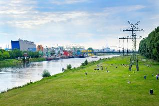 verweist auf: Umwelt und Gesundheit konsequent zusammendenken – Kurzfassung Landschaftsfoto mit Industrieanlage, Fluss und grüner Liegewiese (verweist auf: Umwelt und Gesundheit konsequent zusammendenken – Kurzfassung)